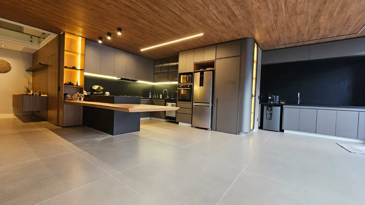 Cozinha integrada com armários cinza, forro amadeirado, ilha com tampo de madeira e LED