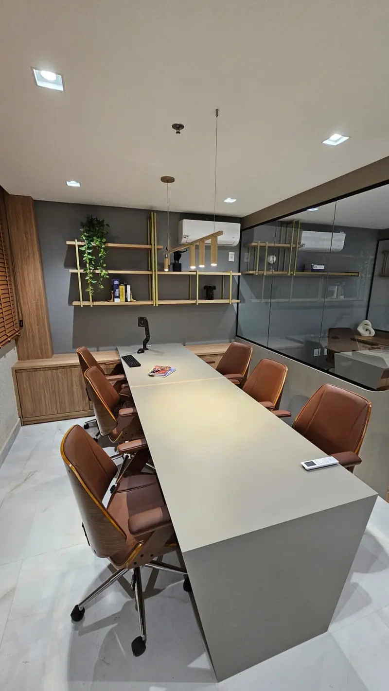 Escritório com mesa de reunião, cadeiras de couro e estantes metálicas com madeira