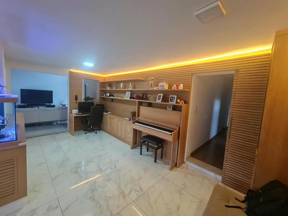 Sala integrada com escritório, estante iluminada e ripado amadeirado